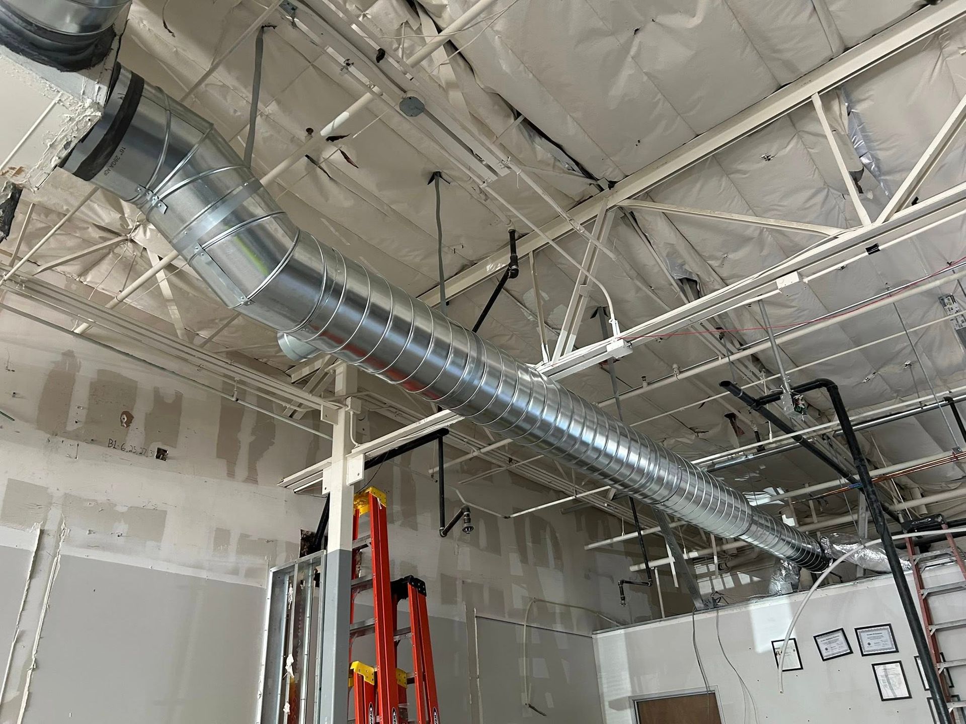 Industrial interior with exposed ceiling ducts, beams, and hanging lights in a construction space