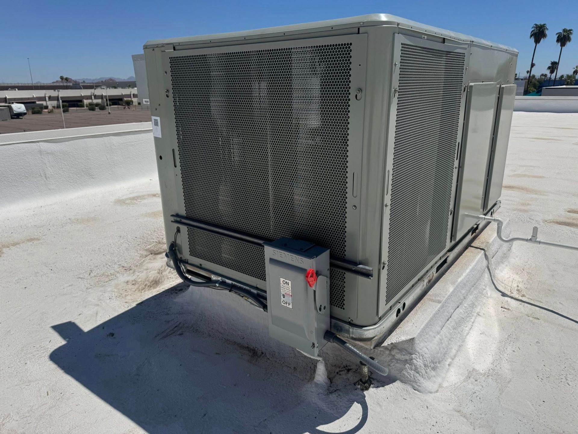 Large rooftop HVAC unit on a flat roof beside a small control box and cable conduit.