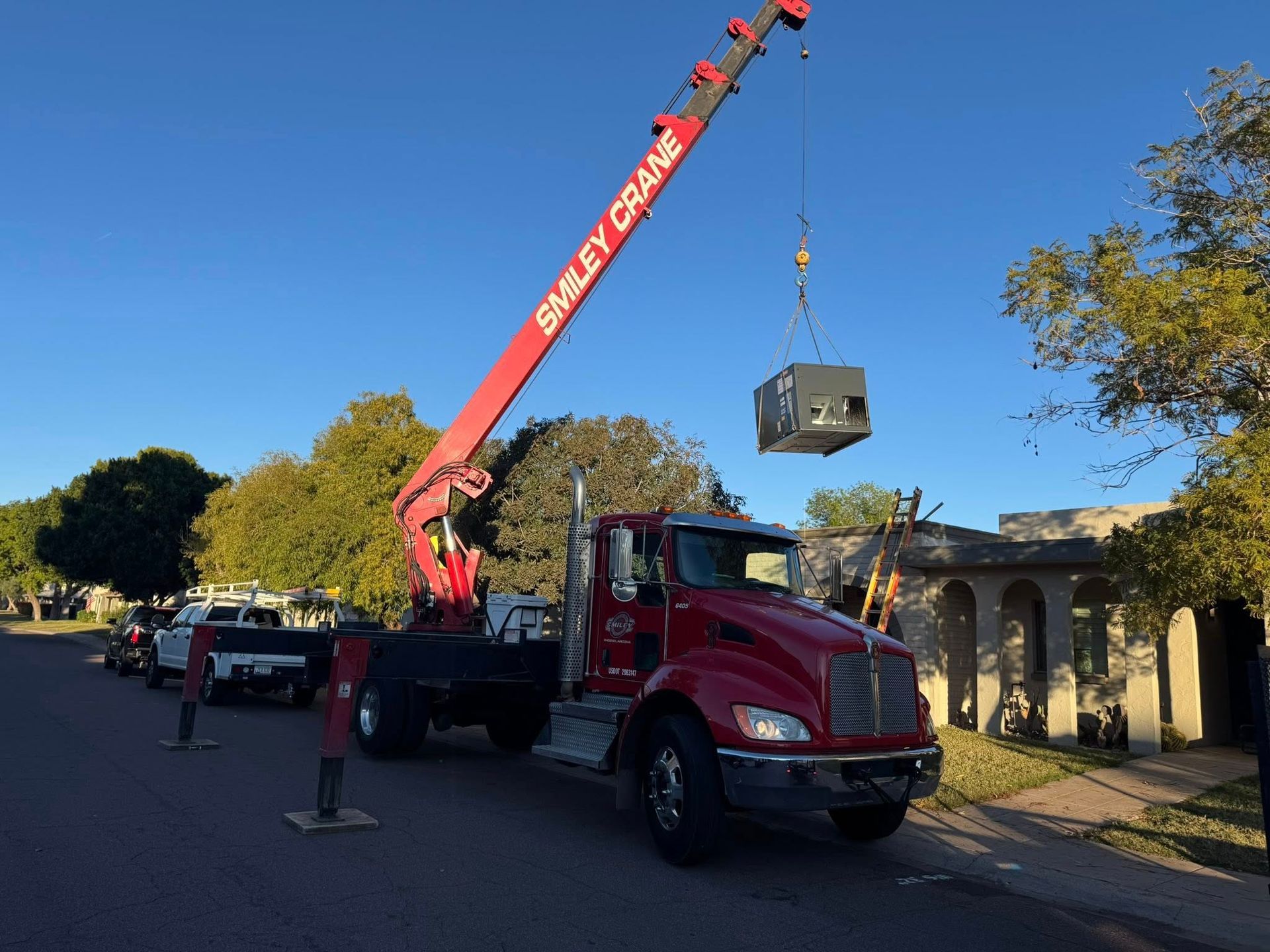 Crane truck lifting a large HVAC unit on a suburban street at sunset