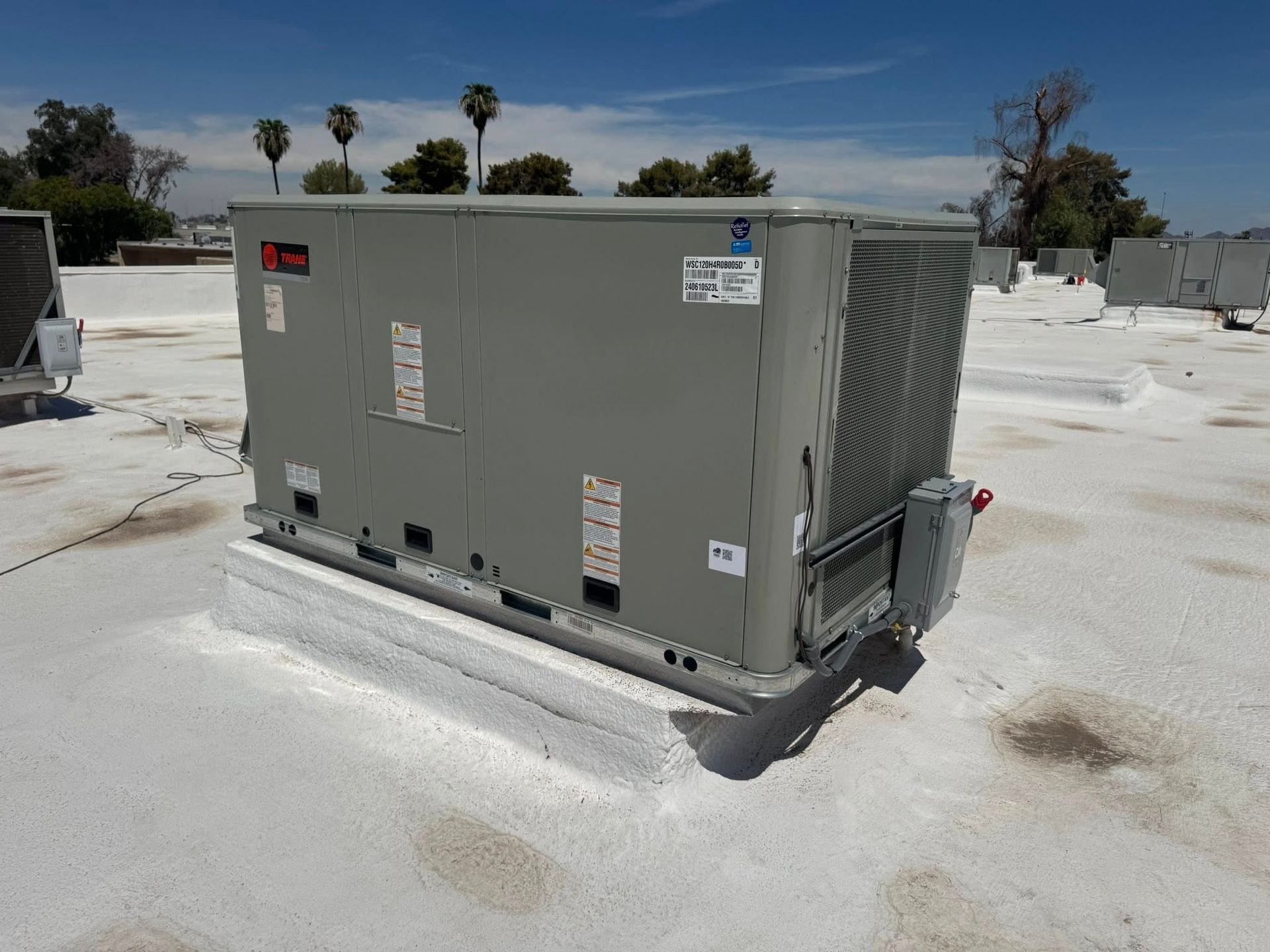 Gray rooftop HVAC unit on a flat roof under a sunny sky with palm trees in the background