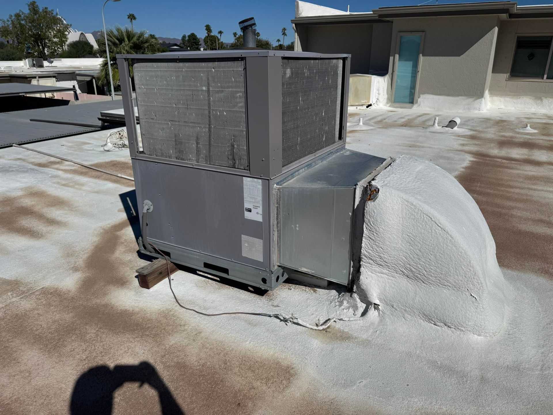 Emergency HVAC repair on unit outdoors with a mound of white foam or insulation spilling beside it on a rooftop.