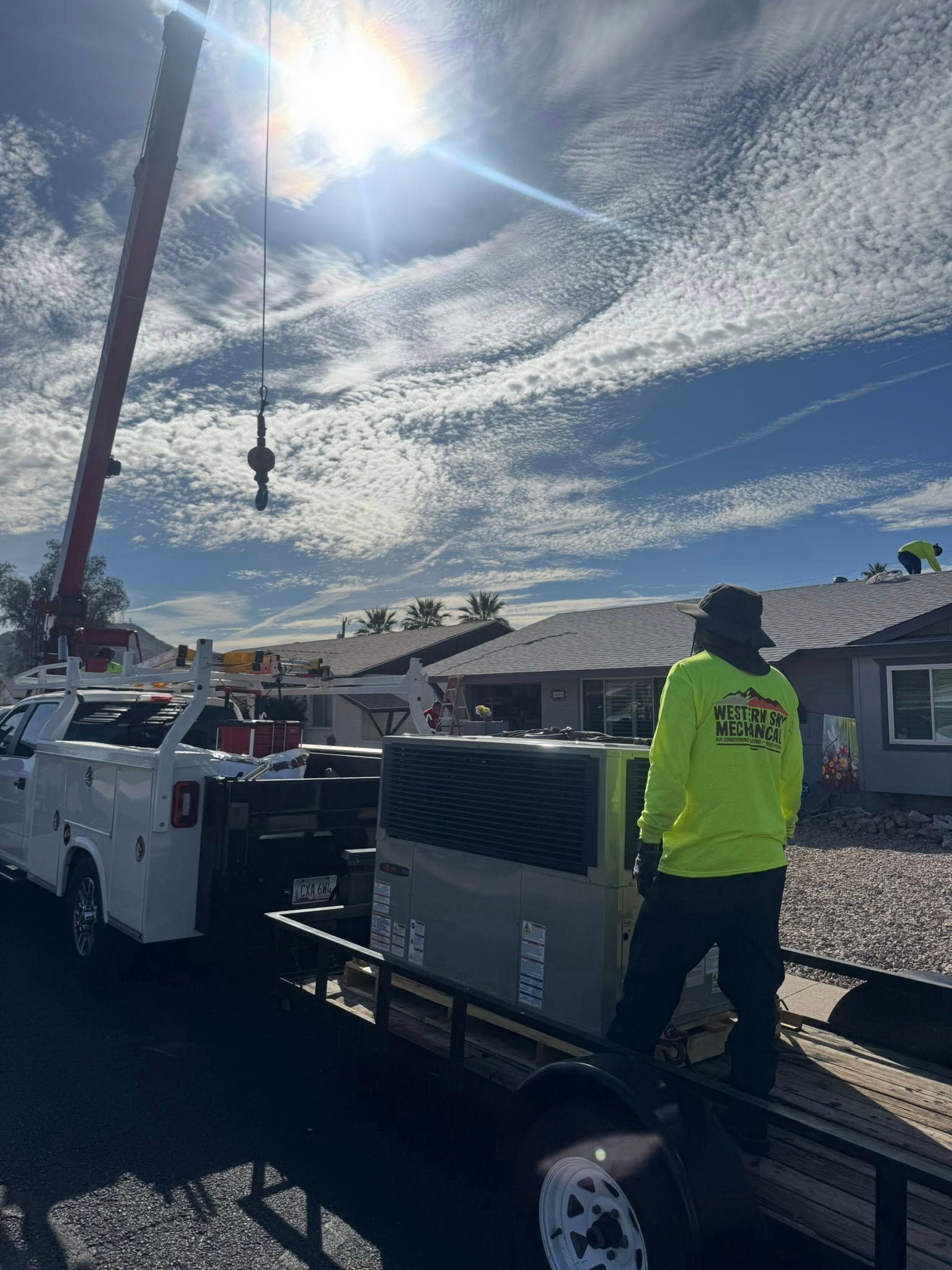 Tow truck and worker on a sunny residential street, lifting a AC unit to a commercial roof in Phoenix AC