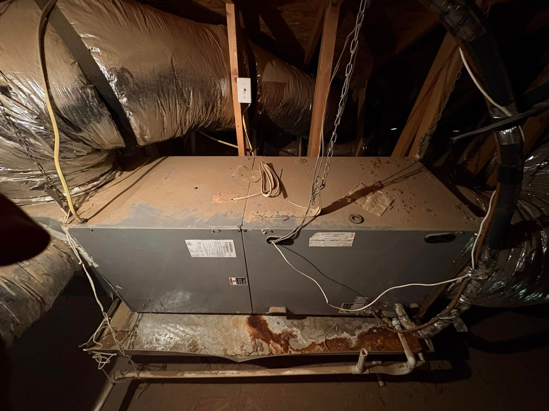 Exposed HVAC ductwork and metal furnace unit in a dim attic, with insulation lining the ceiling