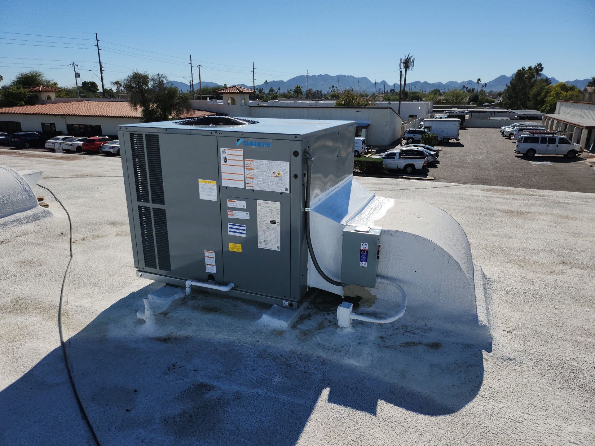 Rooftop HVAC unit beside a white cylindrical tank on a flat roof, with a parking lot and distant mountains behind Phoenix AZ