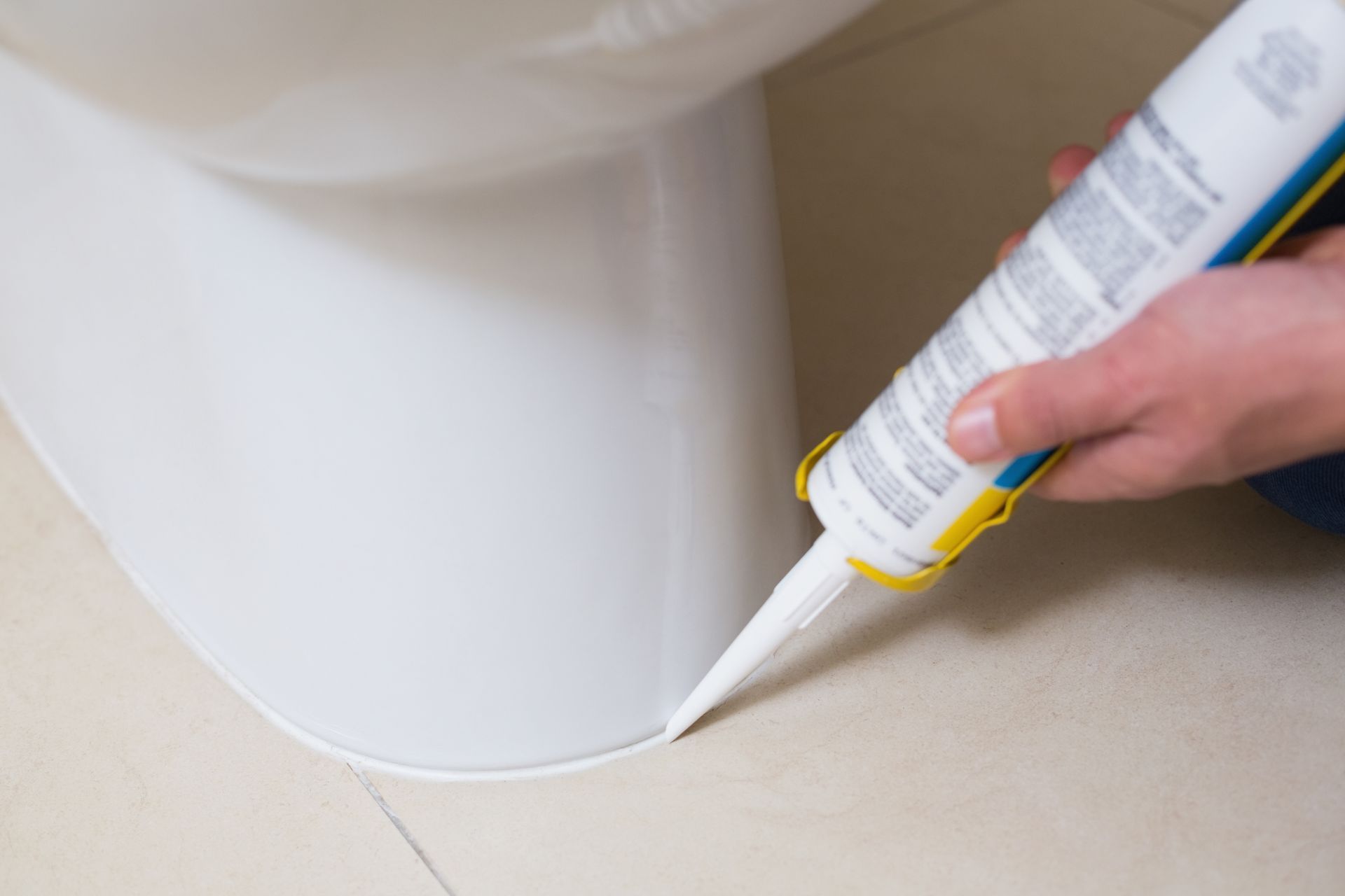 A person is applying caulk to the bottom of a toilet.
