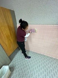A woman is cleaning a pink tiled wall in a bathroom.