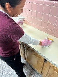 A woman is cleaning a kitchen counter with a cloth and spray bottle.