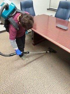 A man is using a vacuum cleaner to clean the carpet in a conference room.