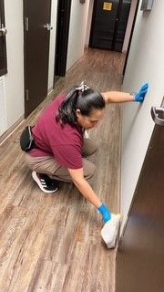 A woman is kneeling down in a hallway cleaning the floor.