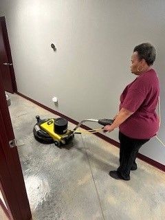 A woman is cleaning the floor with a machine in a hallway.