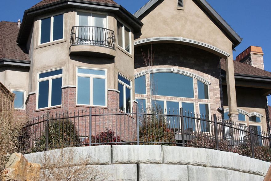 Two-story house with brick and stucco exterior, arched windows, balcony, and retaining wall.