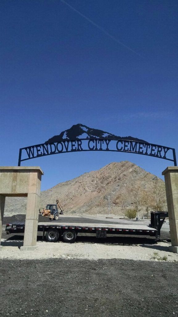Entrance to Wendover City Cemetery under a blue sky, with mountain backdrop and a flatbed trailer.