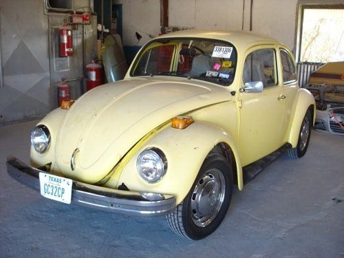 A yellow volkswagen beetle is parked in a garage