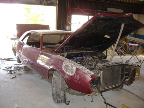 A red car with the hood up is sitting in a garage.