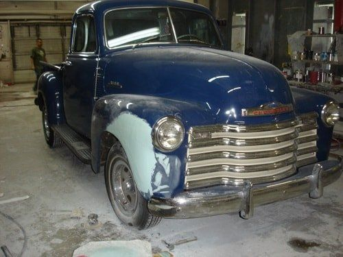An old blue truck is being restored in a garage.