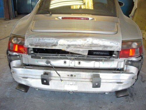 A silver car with a broken bumper is sitting in a garage