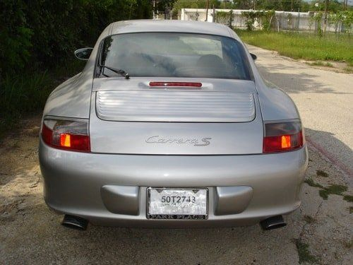 A silver porsche carrera s is parked on a dirt road