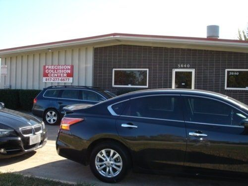 A black car is parked in front of a building that says precision collision center.