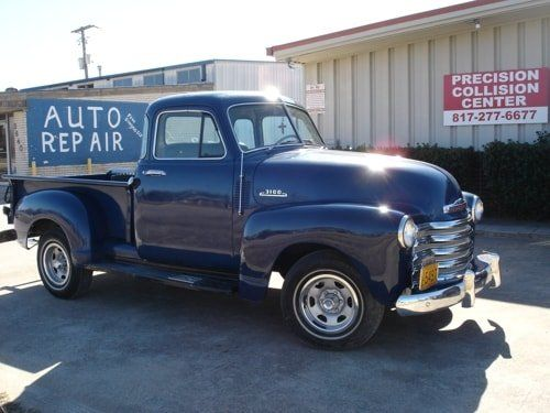 A blue truck is parked in front of a building that says auto repair