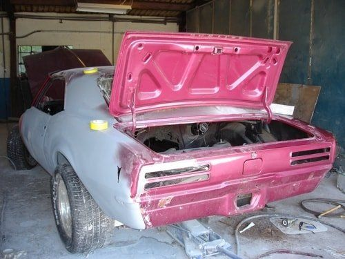 A pink car with the hood open is sitting in a garage.