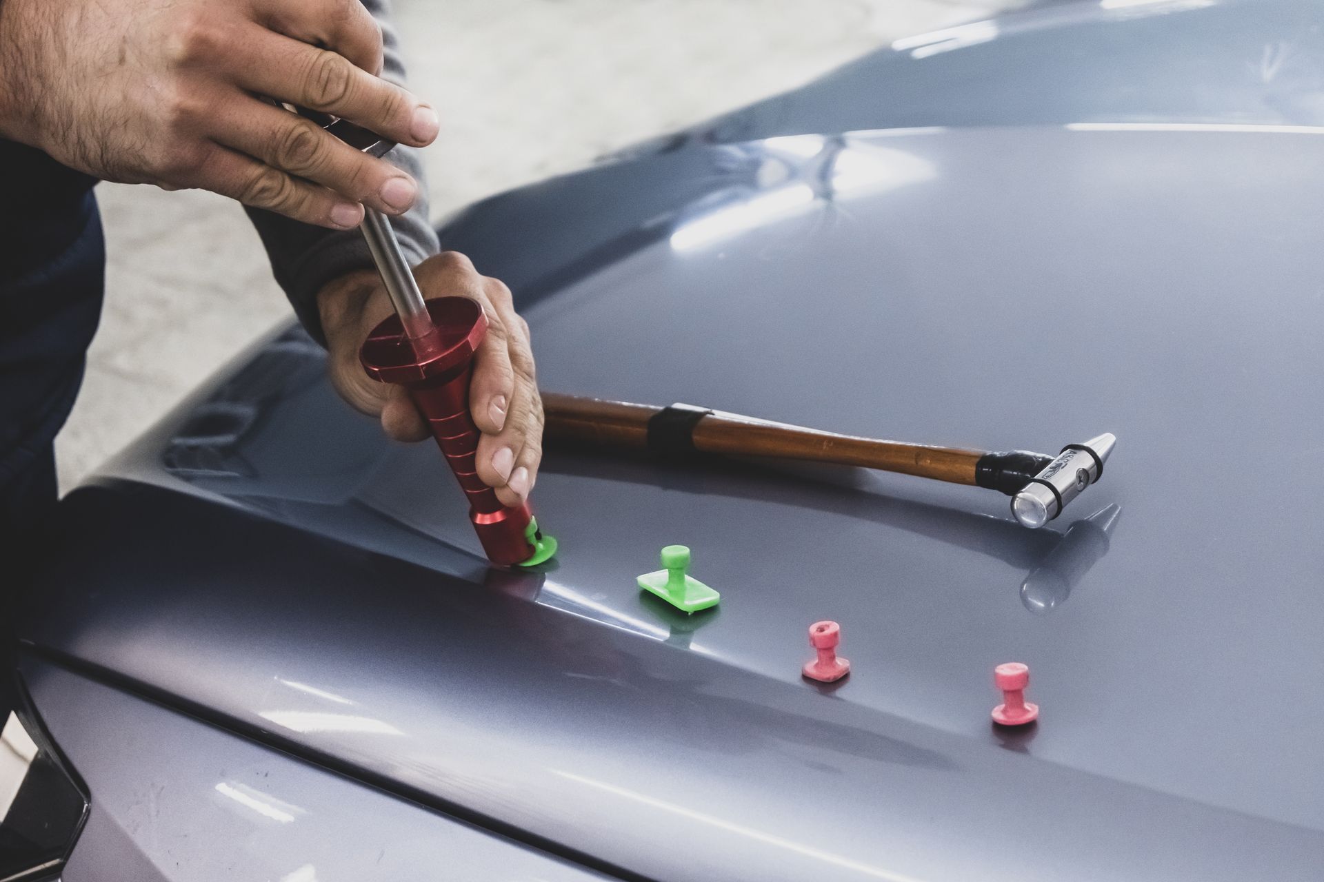 A man is working on the hood of a car with a hammer.