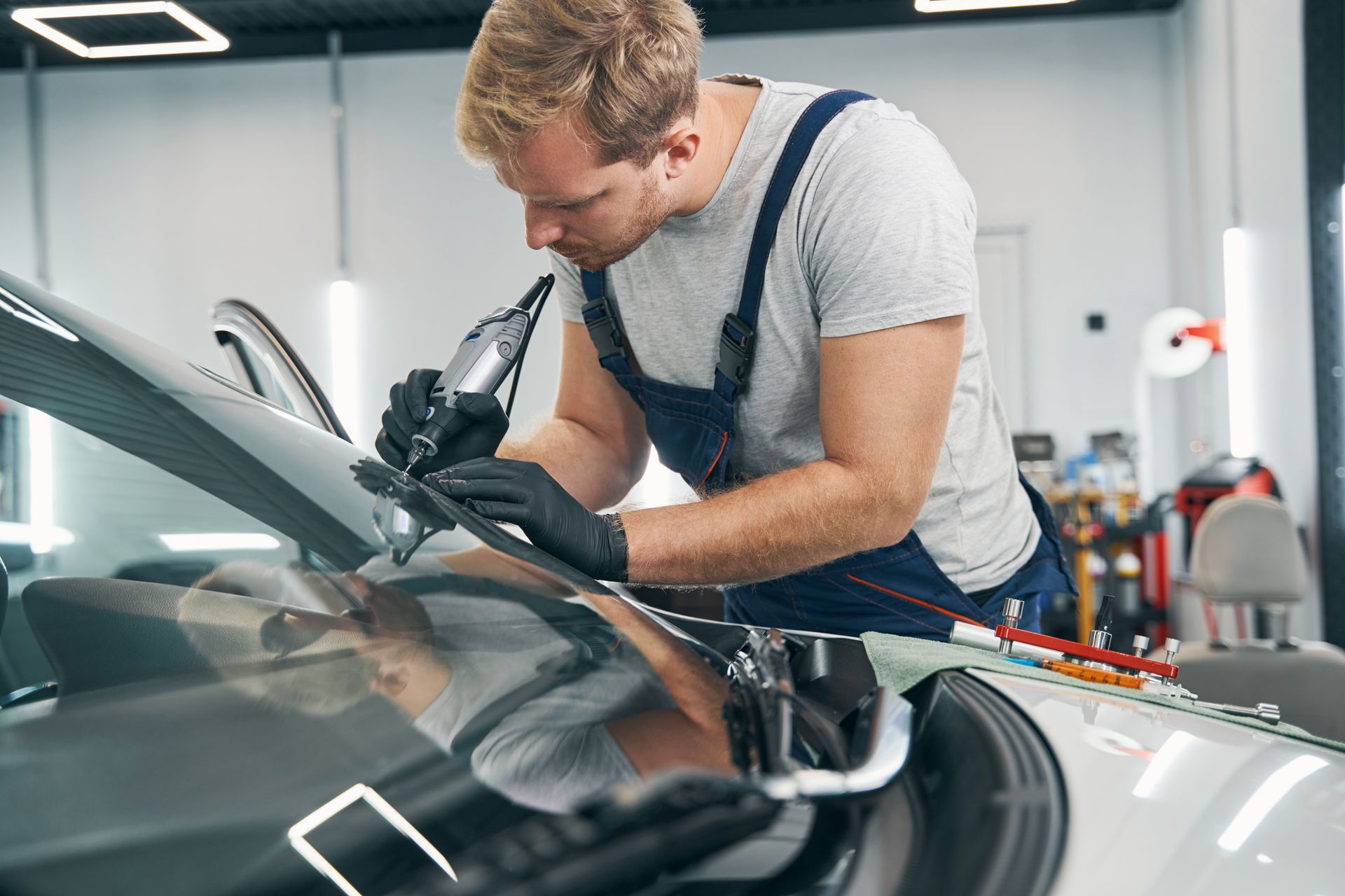A man is fixing a windshield on a car in a garage.