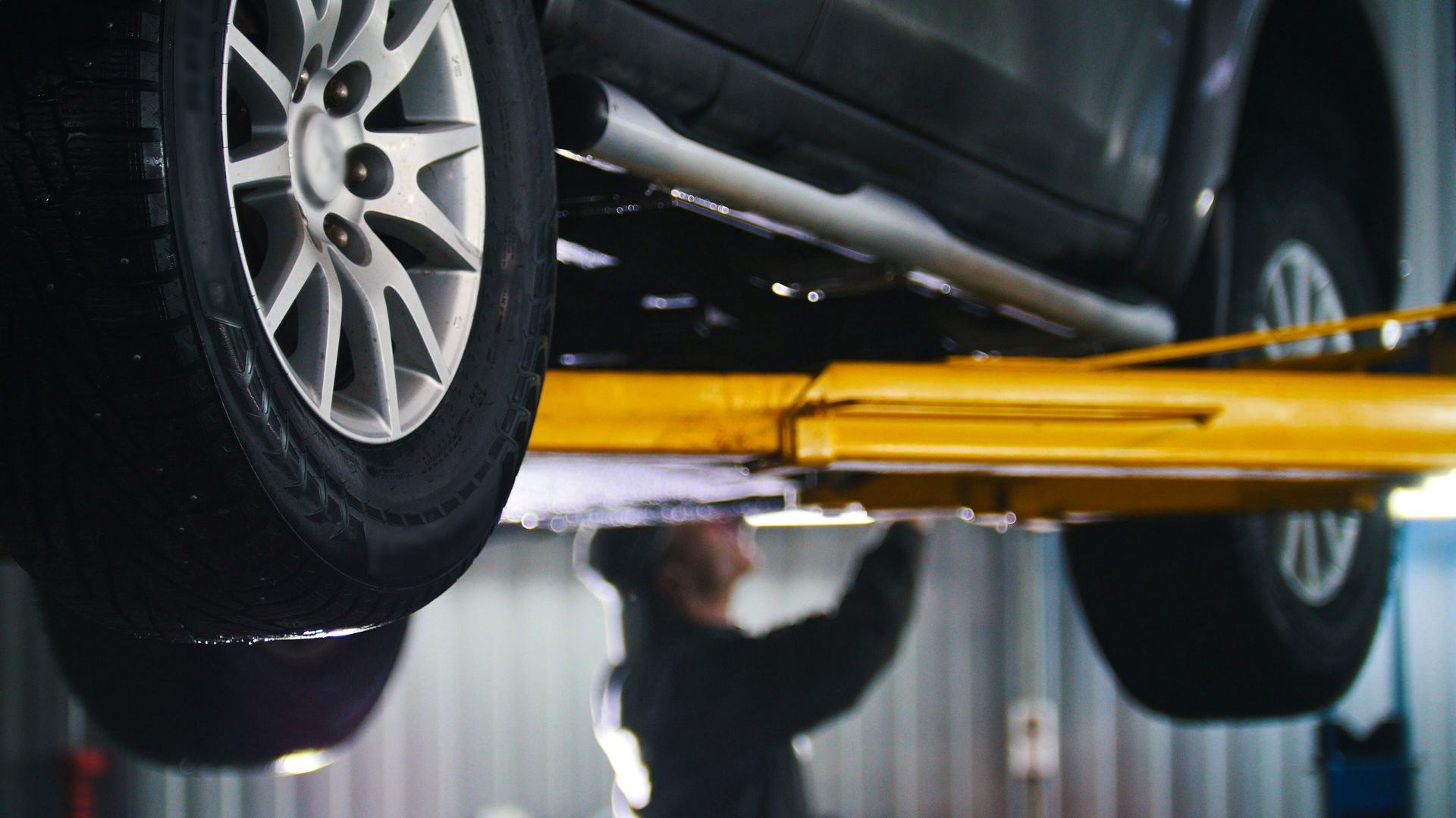 A man is working on a car on a lift in a garage.