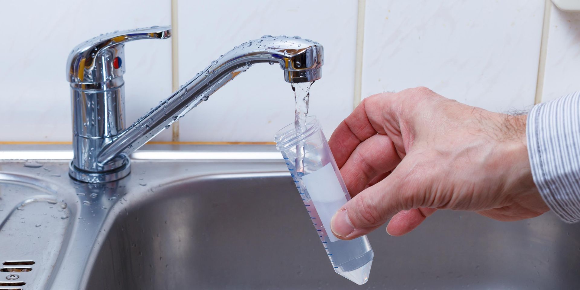 A person is pouring water into a test tube in a sink.