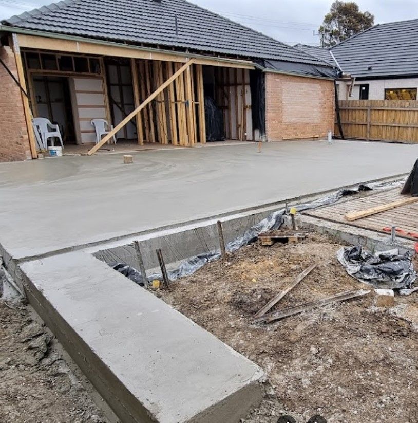 A concrete driveway is being built in front of a house under construction.