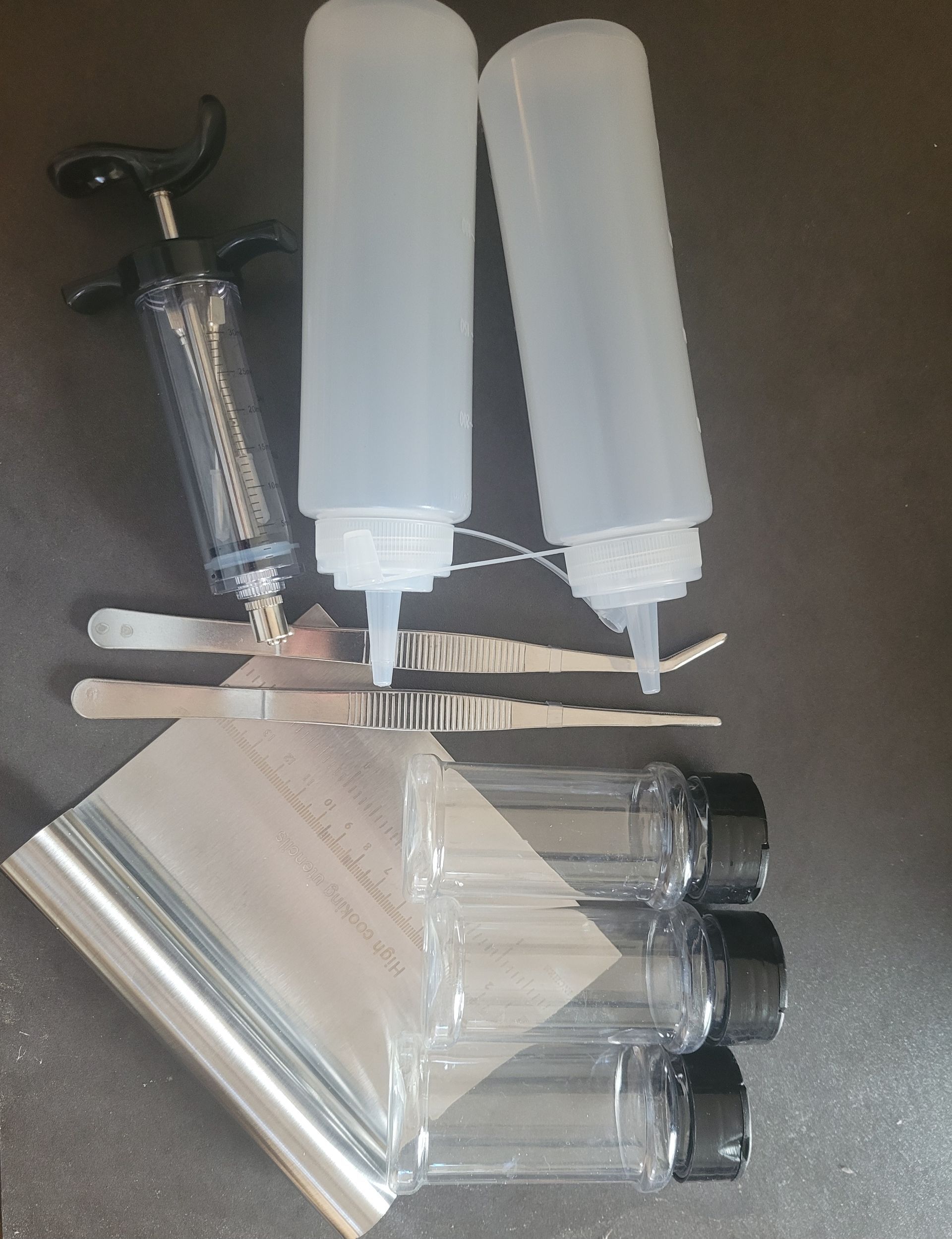Drie afgesloten doorzichtige kruidenpotjes,2 sausflesjes, een injectiespuit, vleespincetten en een plank schraper.
