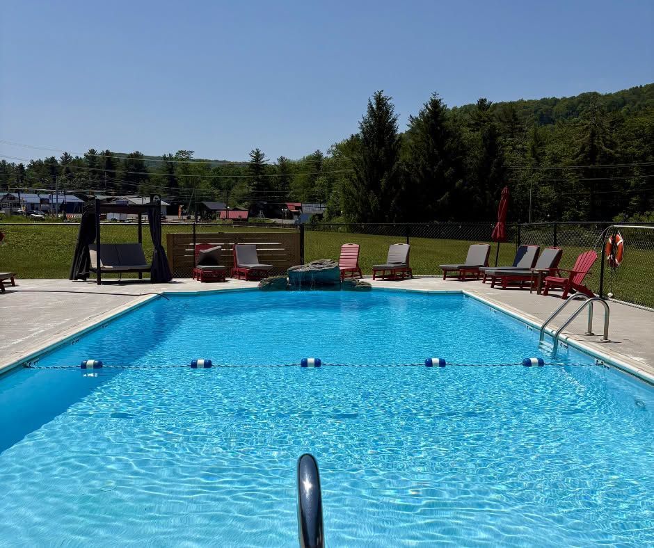 Outdoor swimming pool with blue water, lounge chairs, and a grassy hill in the background