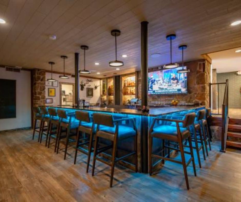 Modern bar with blue-upholstered stools, wood floors, and a wall-mounted TV in warm lighting