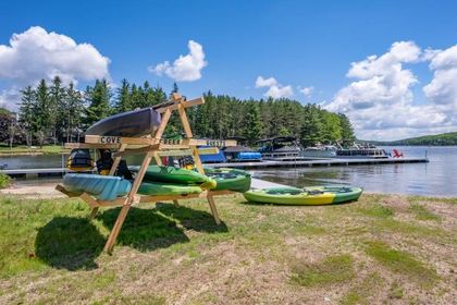 Canoes and kayaks stacked on a wooden rack beside a lakeside dock under a bright blue sky