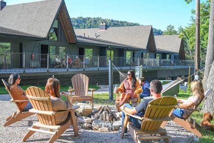 People sitting in Adirondack chairs around a fire pit at a lakeside lodge