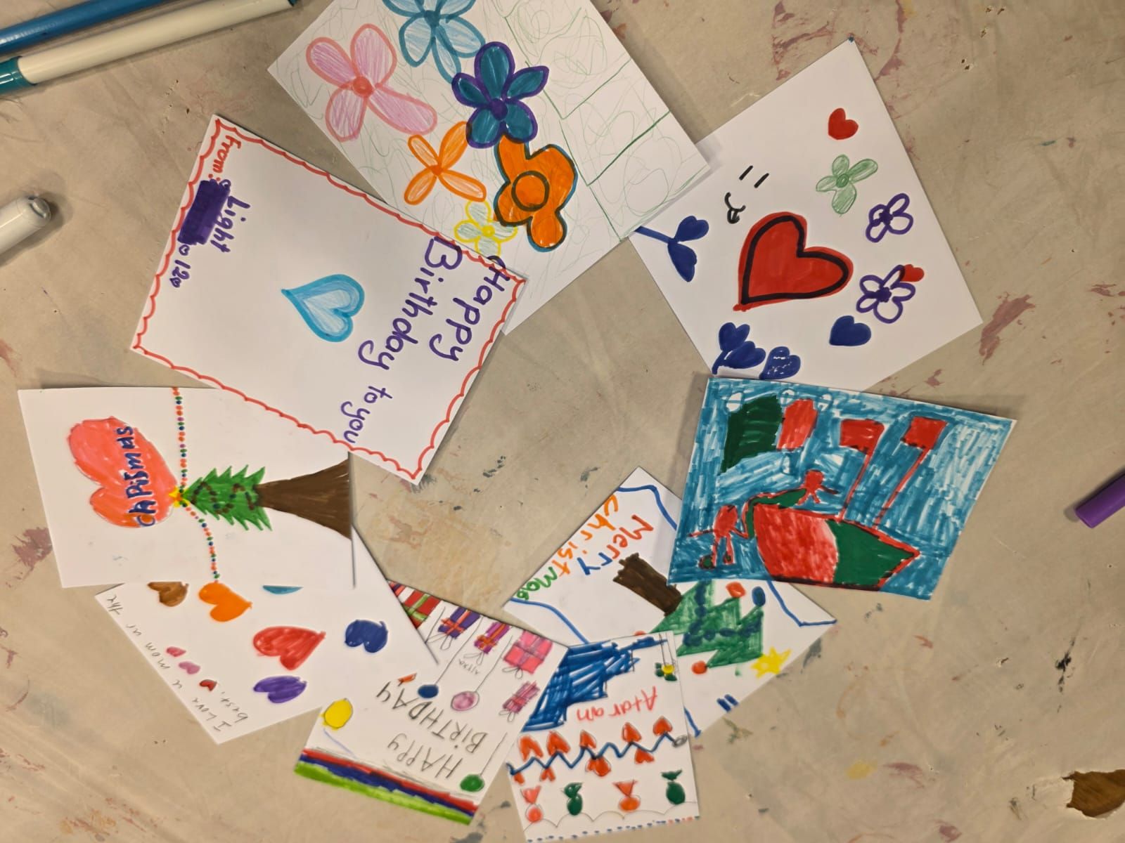Hand-drawn birthday cards arranged in a circle. Decorated with flowers, hearts, and greetings in various colors.