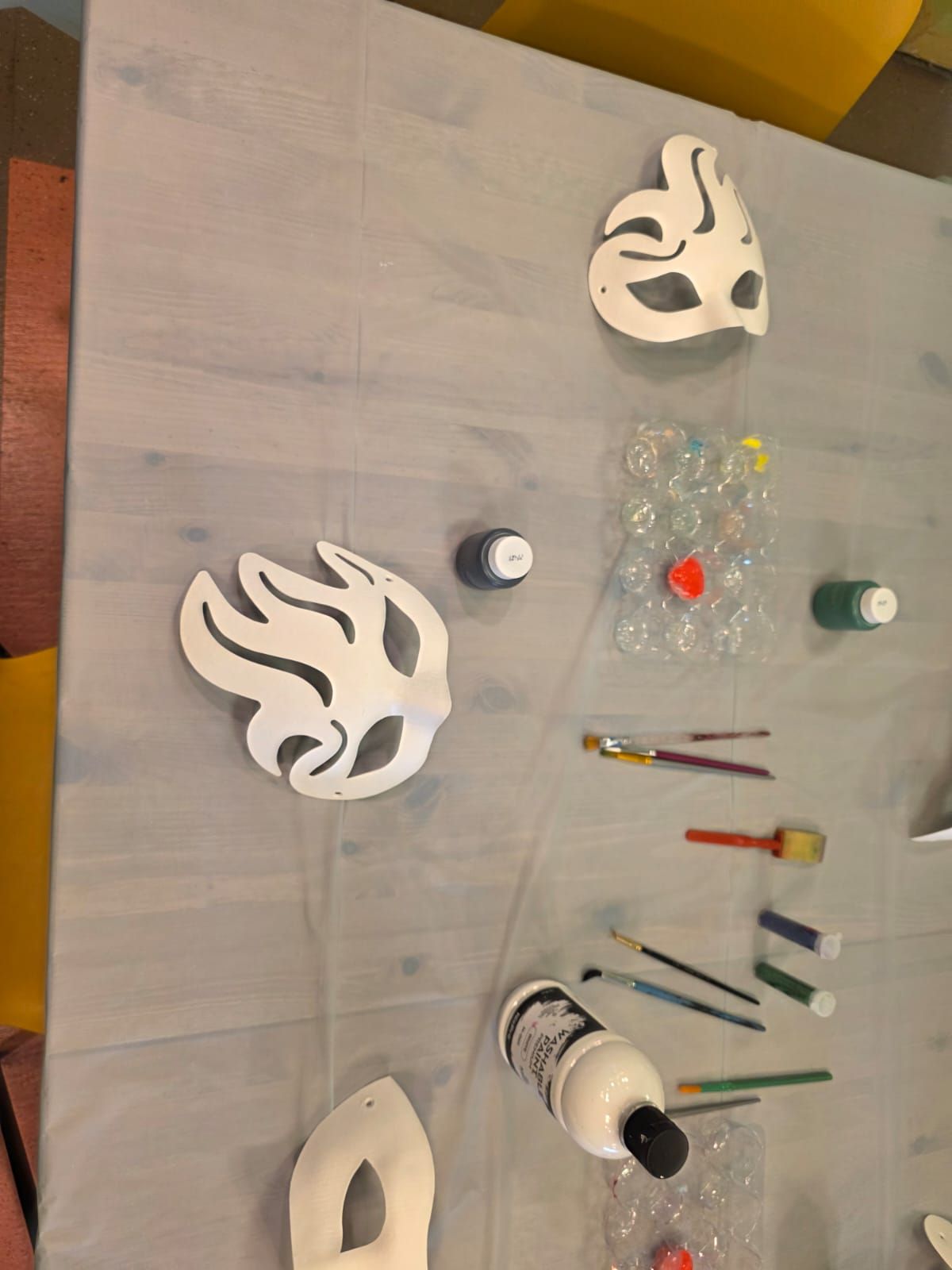 Craft supplies on a table: white masks, paint, brushes, and plastic bottles.