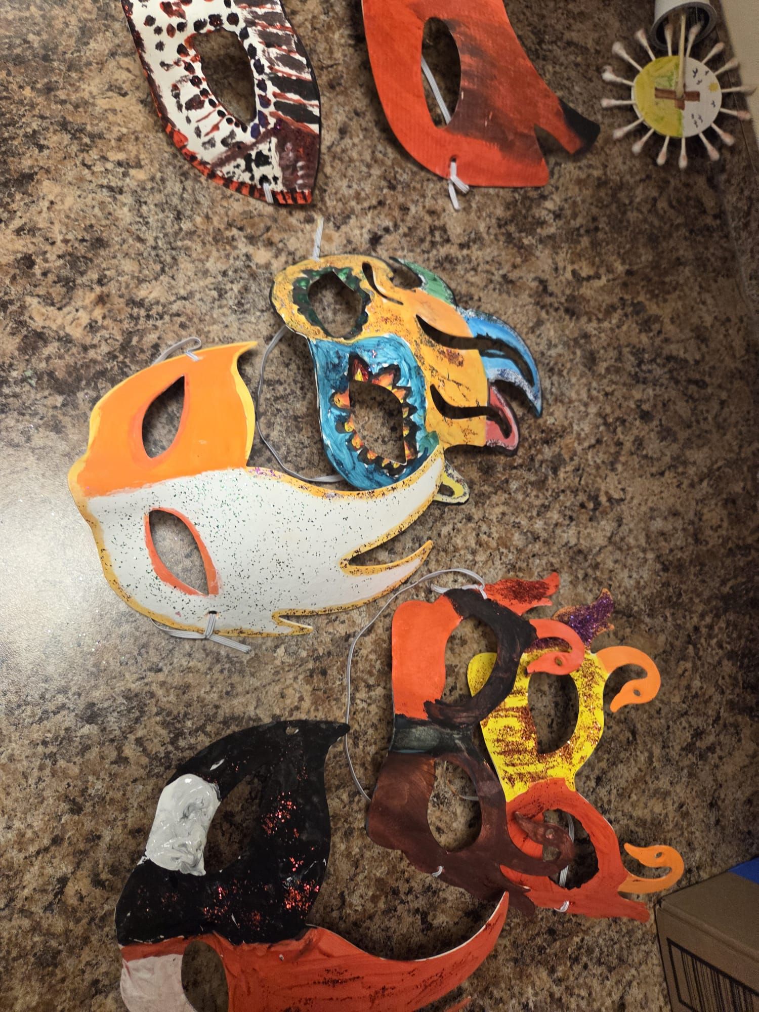 Colorful, decorated masks hanging on a wall. Various shapes and designs, including feathers and sun.