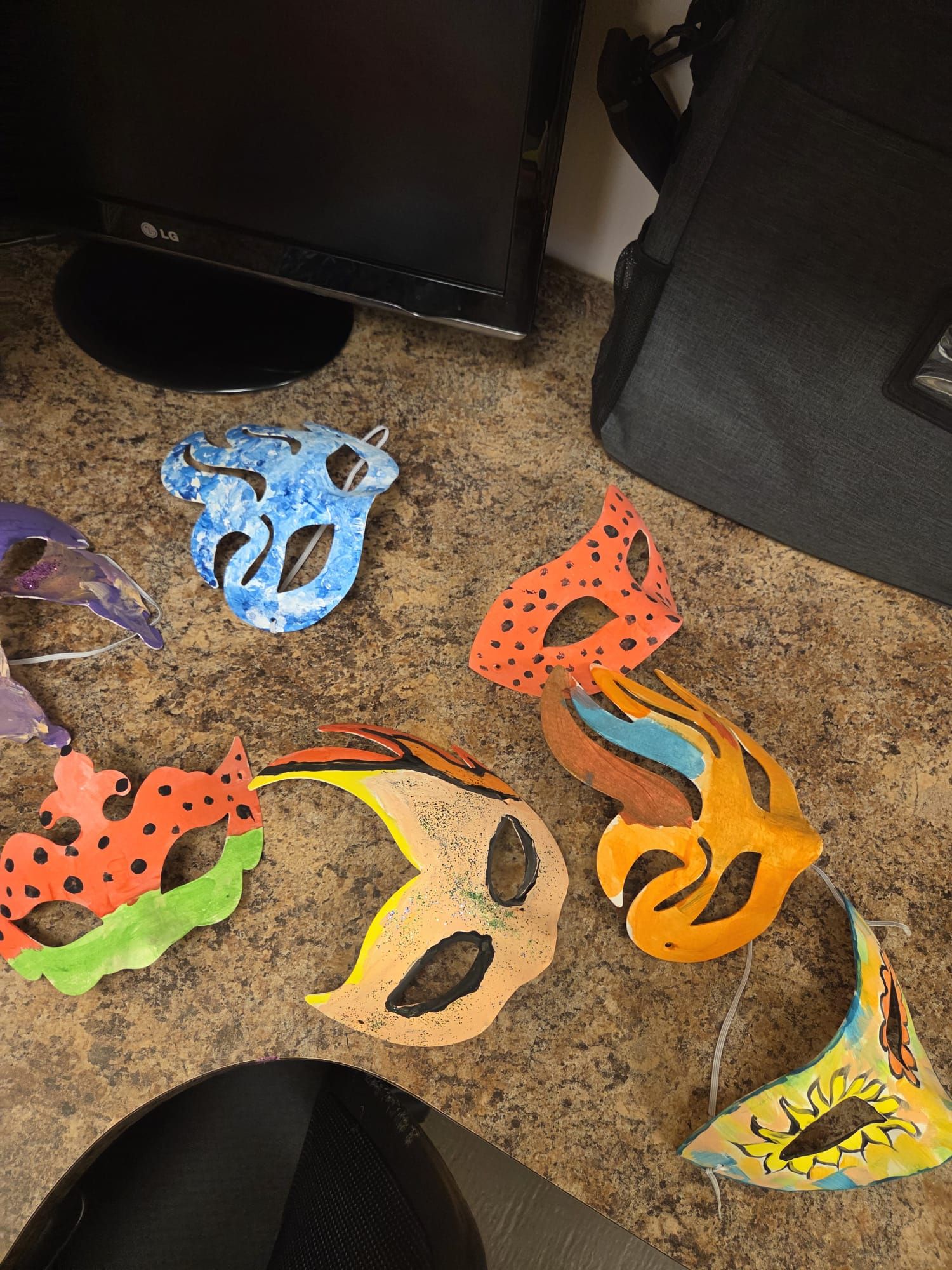 Colorful, handmade masks on a surface. Different shapes and painted designs; blue, orange, and green are visible.