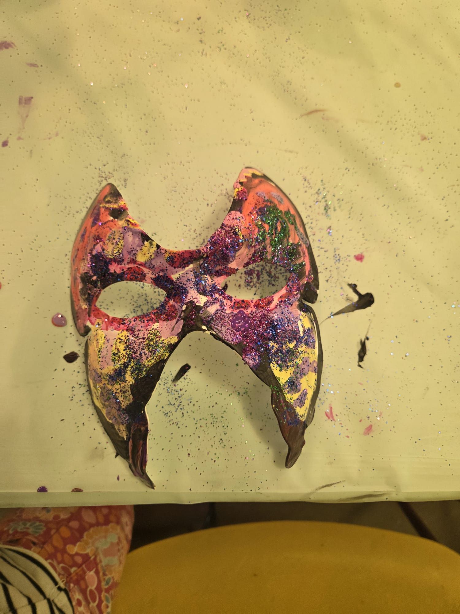Colorful painted mask with glitter on a white surface.