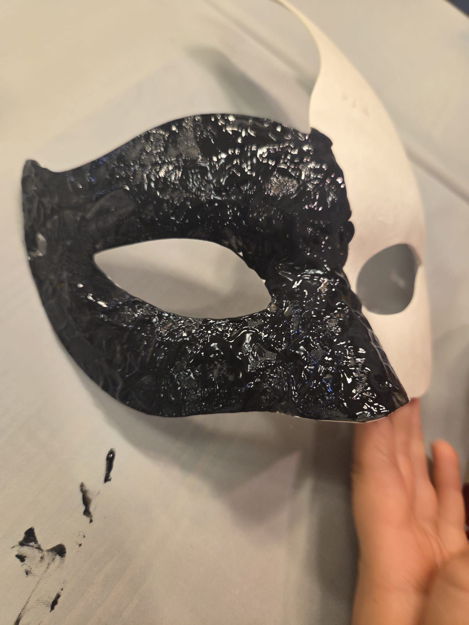 A half-black, half-white mask, with a hand touching the white side, on a white surface.