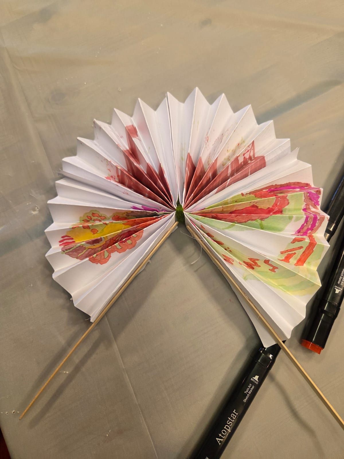 Folded paper fan with floral design, held by two wooden sticks.
