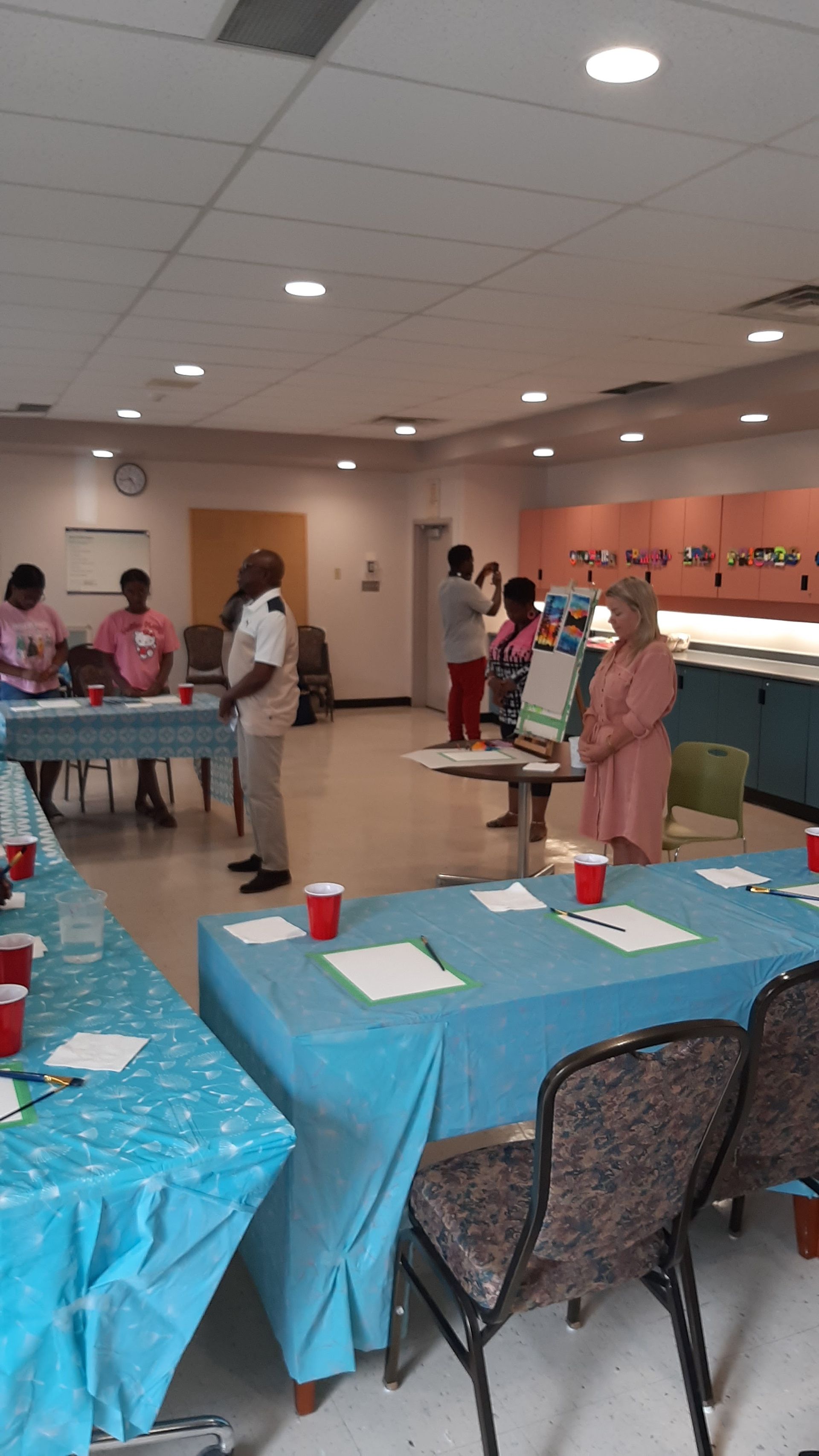 People in a room at tables, possibly a workshop. Pink and blue decor.