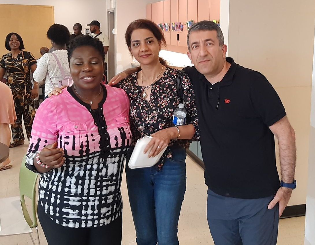 Three people pose for a photo indoors; woman in pink top gives a thumbs up.