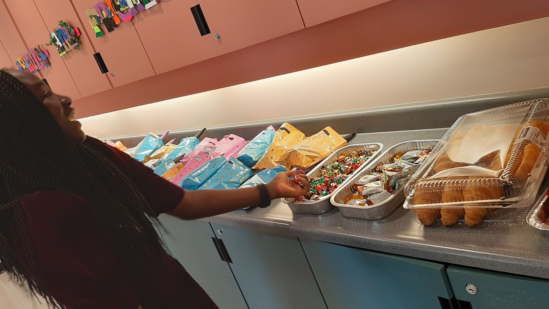 Person reaching for food display, smiling. Snack items in containers on counter.
