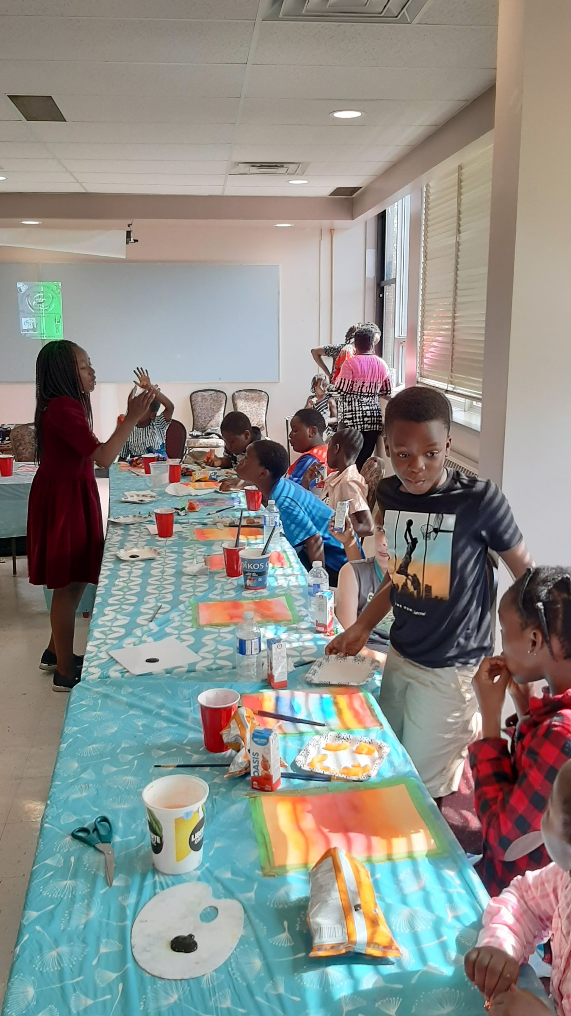 Children painting at a table with an instructor; sunny room.