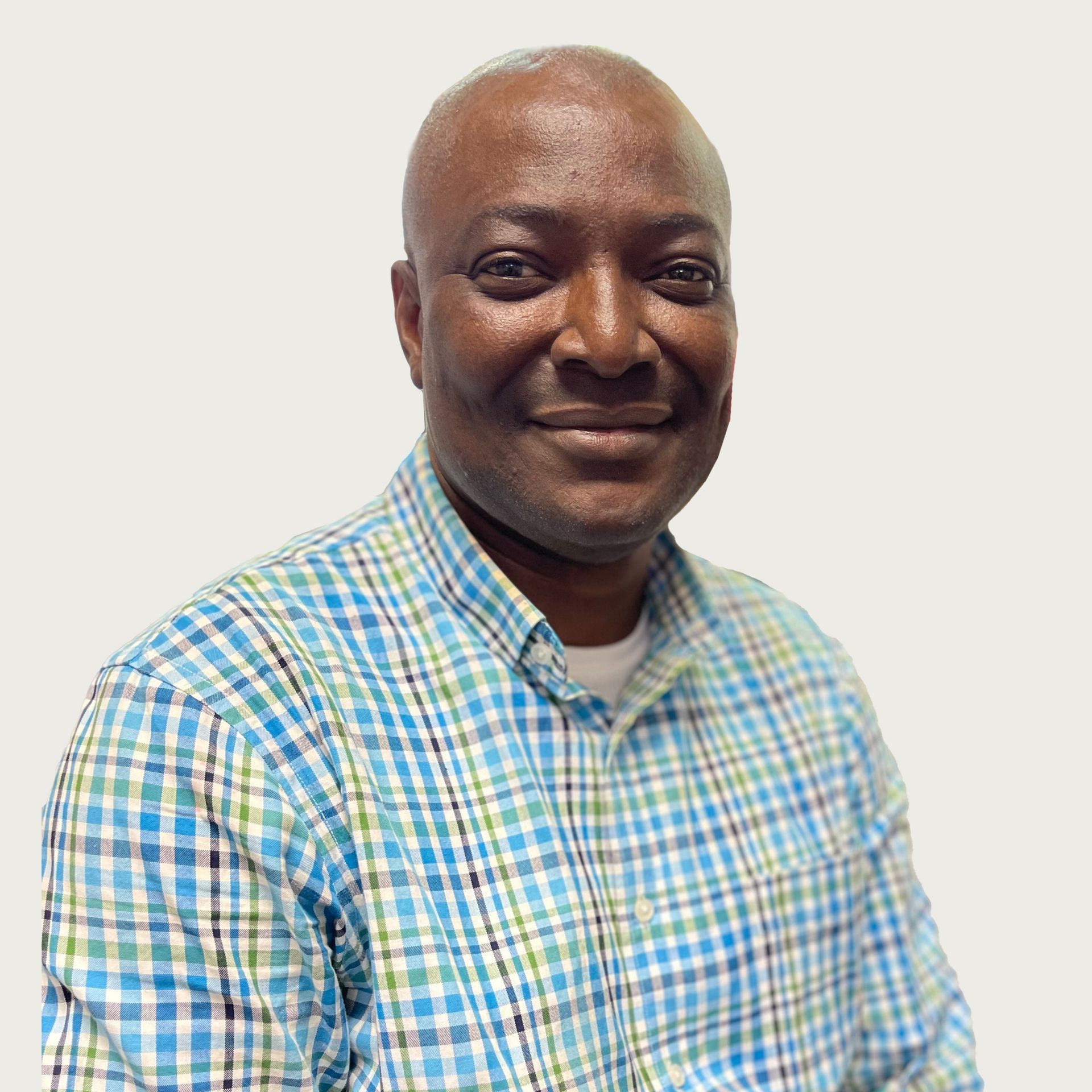 Man in blue and green checkered shirt smiles at the camera against a plain background.