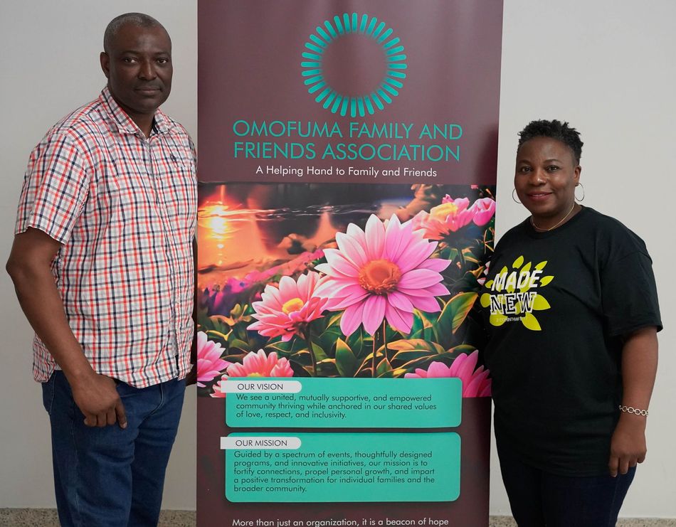 Two people stand beside a banner: man in red plaid shirt, woman in black shirt. Banner reads 