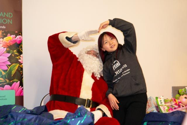Girl poses with Santa, making a heart with her hands. Santa is seated and smiling.
