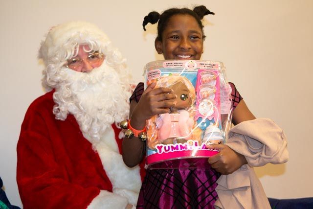 Santa Claus with a smiling girl, holding a doll. Girl wearing a purple dress.