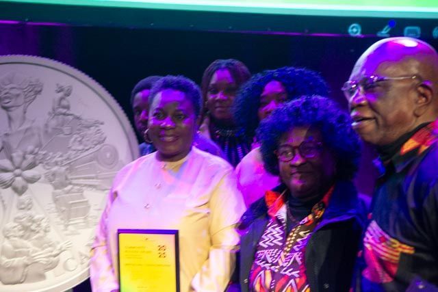 Group of people, Black, celebrating a recent achievement. Holding award. Silver art piece in background.